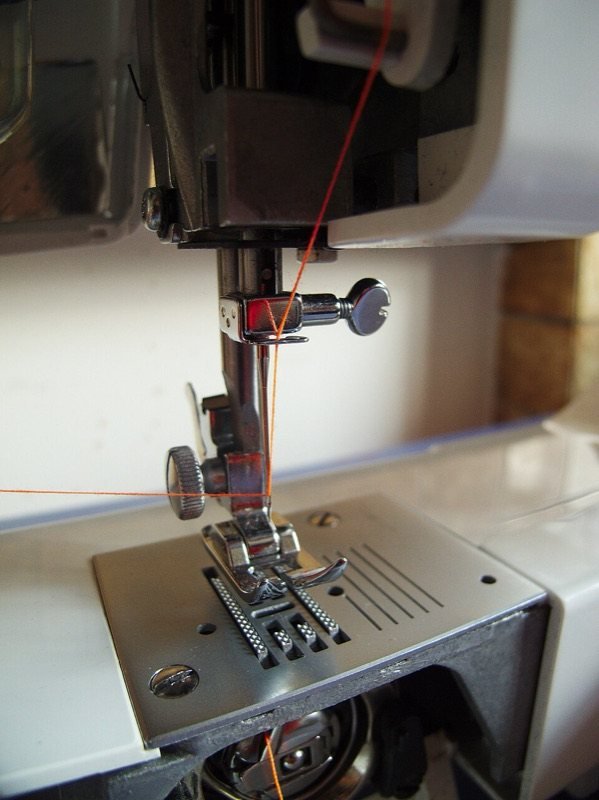 Aguja enhebrada y prensatelas sobre la placa de una máquina de coser